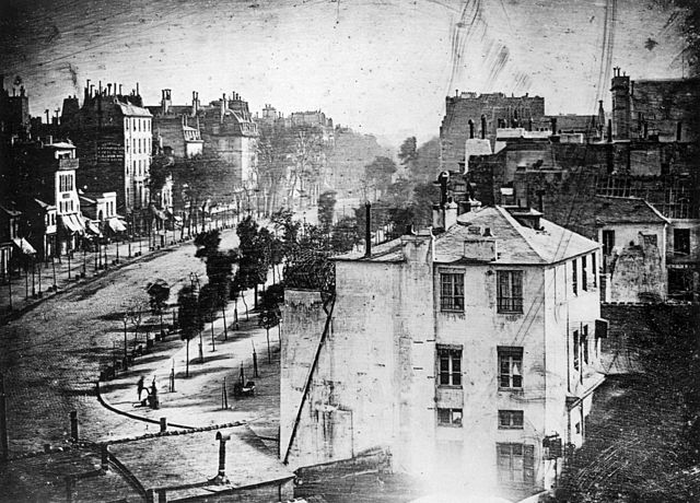 Boulevard du Temple, París, distrito 3, Daguerrotipo.  Realizada en 1838 por el inventor Louis Daguerre, se cree que esta es la fotografía más antigua que muestra a una persona viva.  Es una vista de una calle muy transitada, pero debido a que la exposición duró varios minutos, el tráfico en movimiento no dejó rastro.  Solo los dos hombres cerca de la esquina inferior izquierda, uno aparentemente con sus botas lustradas por el otro, permanecieron en un lugar el tiempo suficiente para ser visibles.  Como ocurre con la mayoría de los daguerrotipos, la imagen es una imagen especular.