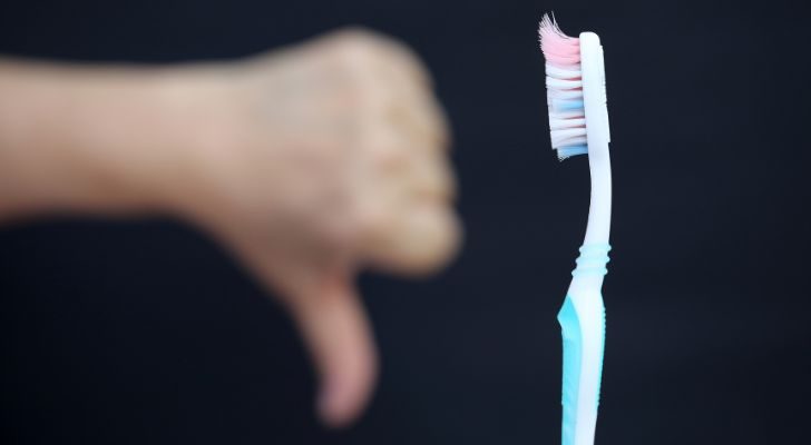 Un viejo cepillo de dientes usado y alguien con el pulgar hacia abajo.